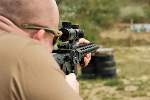 A man is holding an automatic weapon. a man looks into the sight of a militar Stock Photos