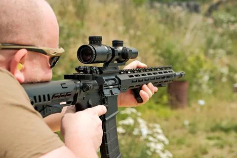 A man is holding an automatic weapon. a man looks into the sight of a militar 写真素材