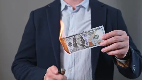 A man is holding a banknote as he ignites one edge with a lighter in a studio 動画素材 338300026