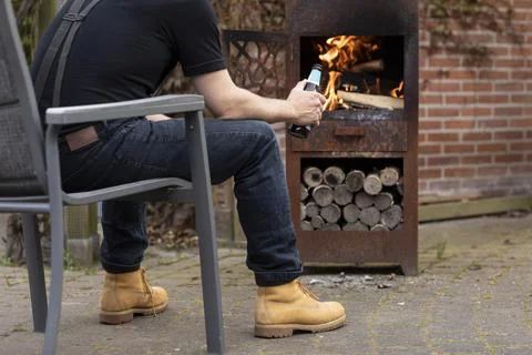 Man holding a beer bottle while sitting outside near a warm fire or wood stove 스톡 사진