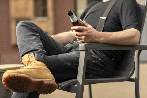 Man holding a beer bottle while sitting in the sun and having a break, relax Stock Photos