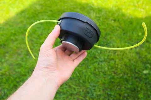 Man holding a black string trimmer head close up on a green grass background Stock Photos