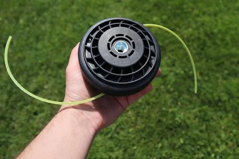 Man holding a black string trimmer head close up on a green grass background Stock Photos