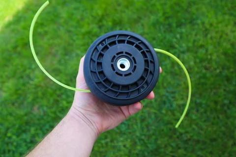 Man holding a black string trimmer head close up on a green grass background Stock Photos