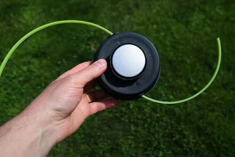 Man holding a black string trimmer head close up on a green grass background Stock Photos