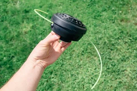 Man holding a black string trimmer head close up on a green grass background Stock Photos