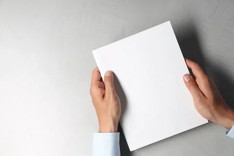 Man holding blank notebook at light grey table, top view. Mockup for design Stock Photos