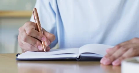 Man holding bronze pen hovering above left page, writing notes and steadying Stock Footage 339652351