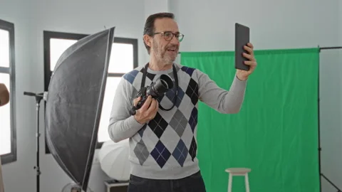 Man holding camera and tablet, right hand raised with tablet toward face an.. Stock Footage 337444172