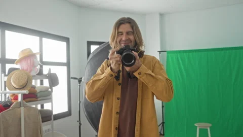 Man holding camera with hands, smiling and pointing lens forward amid green.. Stock Footage 337374655