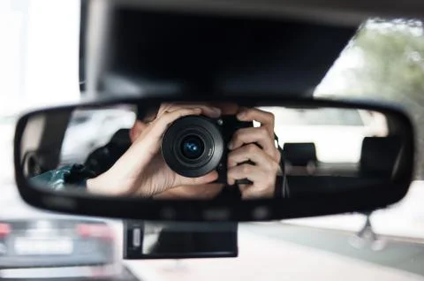 Man holding a camera sits on driver's seat and Looks in the rear-view mirror Stock Photos