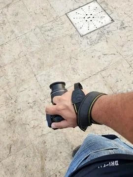 A man is holding a camera with a strap on his wrist, street photography Stock Photos