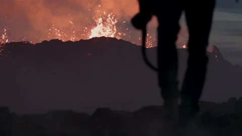 Man holding camera walking away from exploding volcano in background Stock Footage 246782721