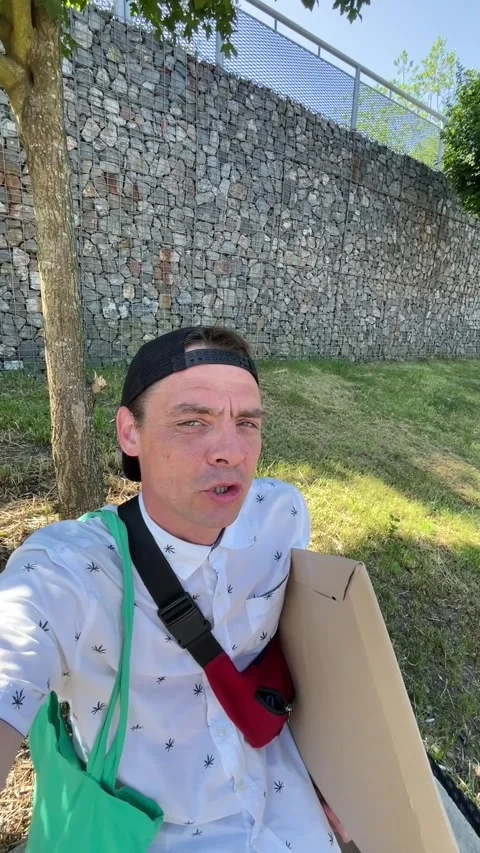 Man holding cardboard box during outdoor errand near gabion retaining wall in Stock Footage 344584273