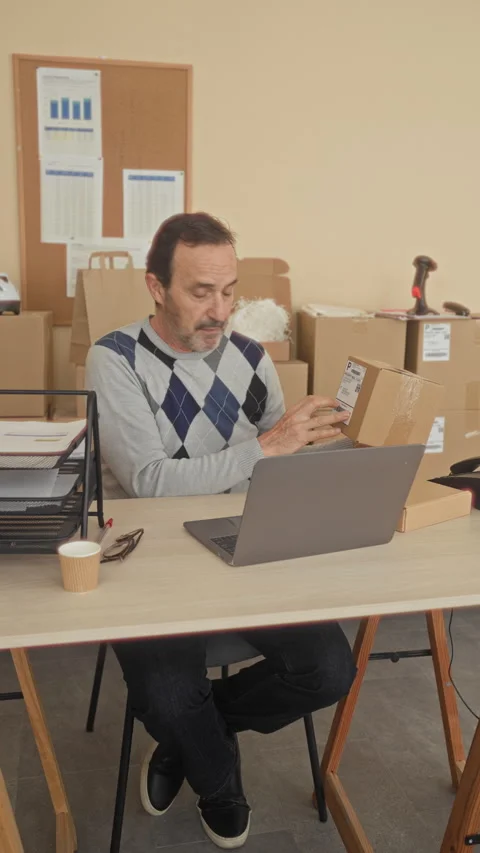 Man holding a cardboard box with one hand and gesturing to a laptop while s.. Video stock 337442413