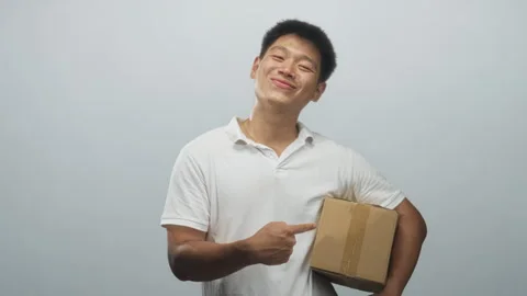 Man holding cardboard box pointing finger at parcel in studio, wearing whit.. Vidéo 339164120