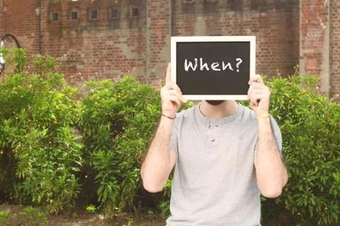 Man holding chalkboard with text "when?" Stock Photos