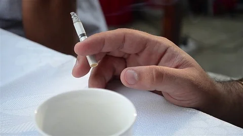 Man holding a cigarette while sitting at a cup of coffee with his friends at Stock Footage 80262927