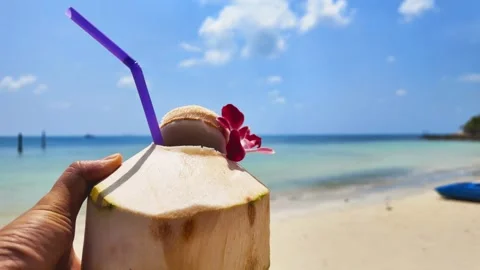 Man holding coconut  with straw walking at seashore. Stockbeeldmateriaal 273771276