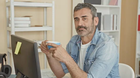 Man holding coffee cup at computer desk in building, seated by monitor and .. 스톡 동영상 337372149