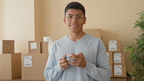 Man holding coffee mug and smiling while standing among stacked shipping bo.. 스톡 동영상 339252594
