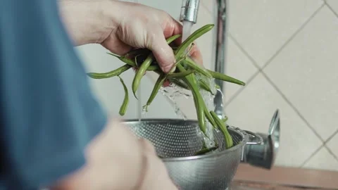 Man holding a colander filled with washed green beans over a kitchen sink Stock Footage 343555527
