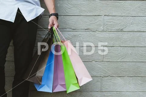 Man holding colorful shopping bag outdoors. shopaholic male standing beside g Stock Photos