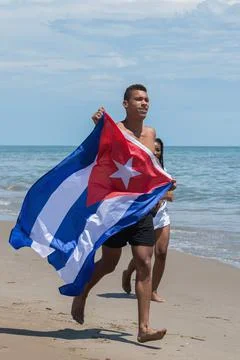 Man holding a Cuban flag while running along the beach. Stock Photos