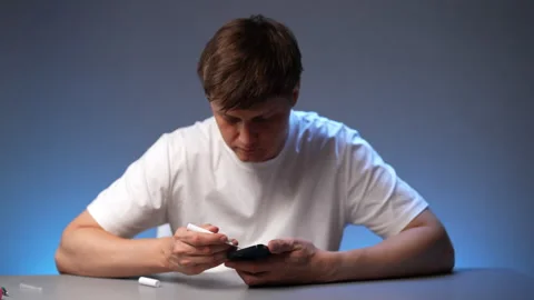 Man holding dark smartphone while using white pen cleaning brush to remove Stock Footage 318519381