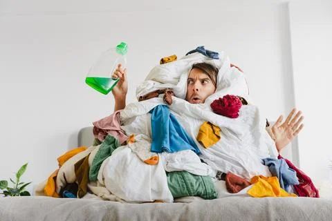 Man Holding Detergent While Trapped in Laundry Clothing Pile Foto stock
