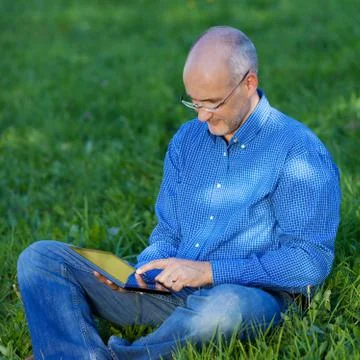 Man holding digital tablet while sitting on grass 스톡 사진