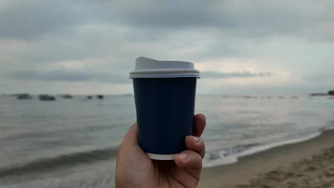 Man holding disposable cup coffee at the beach. Stockbeeldmateriaal 271219280
