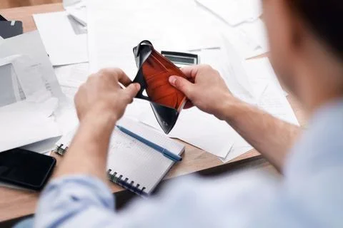 Man holding an empty wallet over a desk with unpaid bills. He faces financi.. 库存照片