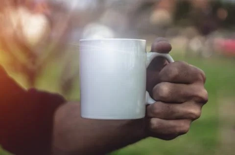 Man holding an empty white cup outdoors, close up. Photos