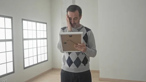 Man holding a framed photo with one hand while touching his cheek with the .. Stock Footage 337442585