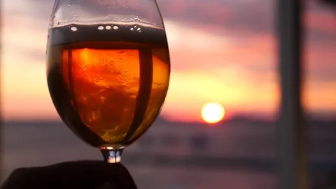 A man is holding a glass of alcohol against the sunset over the sea. close-up Stock Footage