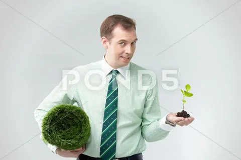 A man holding a grassy rug and a young plant in hands Stock Photos