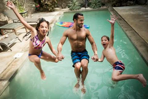 A man holding hands with two children jumping backwards into a swimming pool. Stock Photos
