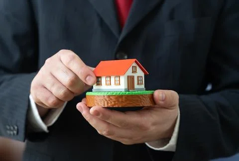 Man holding a house and a plot of land. Real estate for sale. Construction an Stock Photos