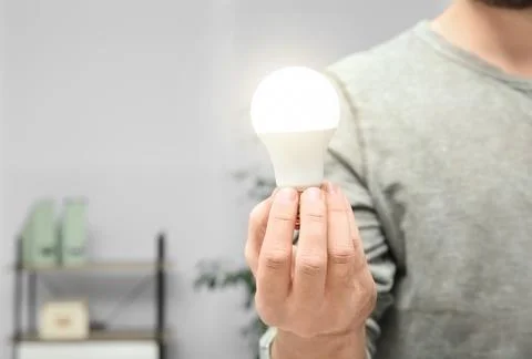 Man holding lamp bulb on blurred background, closeup with space for text Stock Photos