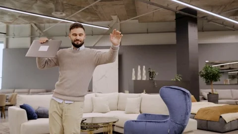 Man holding laptop dancing celebrating success in furniture store Stock Footage 322550131