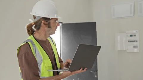 Man holding laptop with hands while typing and looking up, wearing hard hat.. Stock Footage 339195565