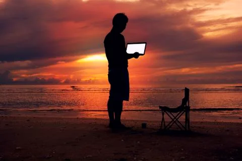 A man holding laptop with white screen on the beach and sunset scene. Stock Photos