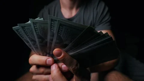 Man Holding a Large Fan of One Hundred Dollar Bills in Dark Interior Stock Footage 339366502