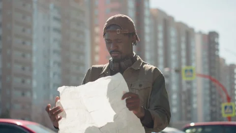Man holding large white paper map examining it closely outdoors with city Stock Footage 345126099