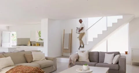 Man holding laundry basket coming down stairs after laundry pickup into bright Stock Footage 335625946