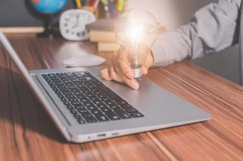 A man holding a light bulb in front of a computer Stock Photos