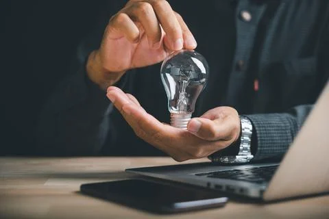 Man holding a light bulb in his hands above a laptop and phone. Idea, innov.. 写真素材