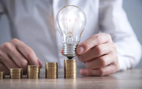 Man holding light bulb. Stack of coins on the desk. Saving energy and money Stock Photos