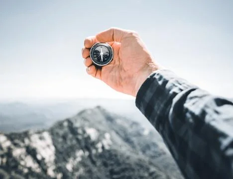Man holding magnetic compass in front of summer mountains, pov. Stock Photos